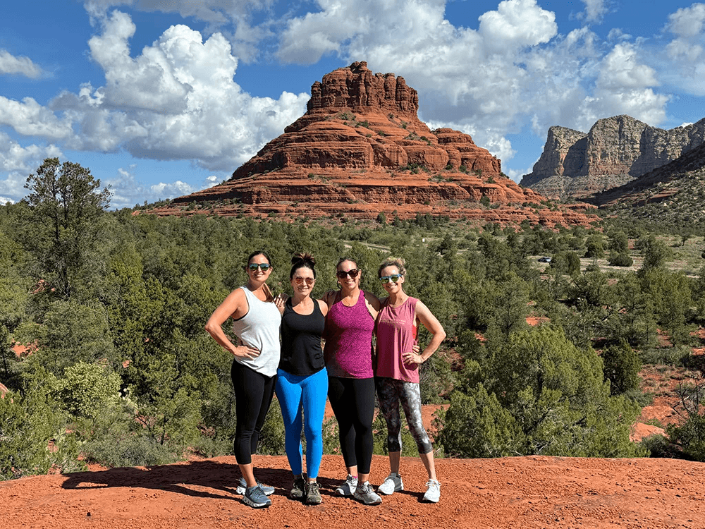 Four friends pose together in front of a red rock formation under a partly cloudy sky.