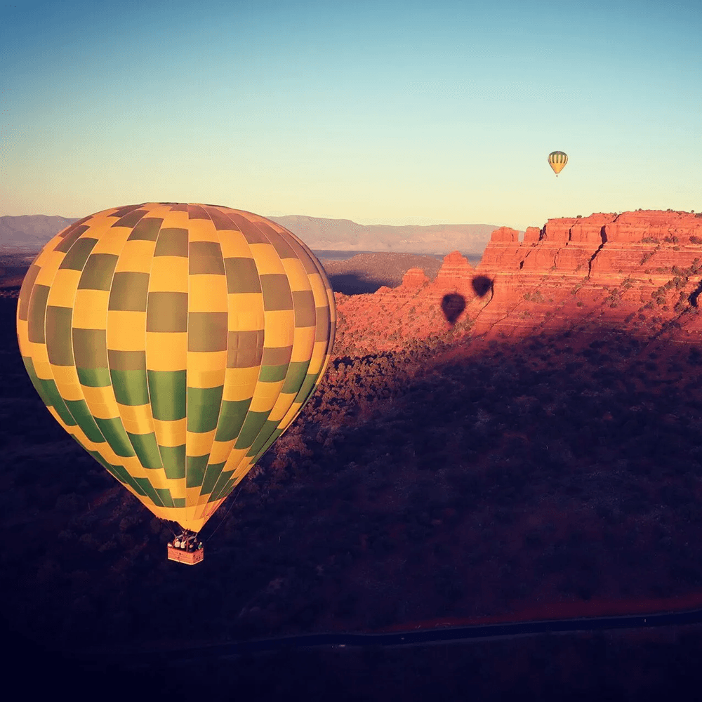 A colorful hot air balloon floats over red rock formations at sunrise.