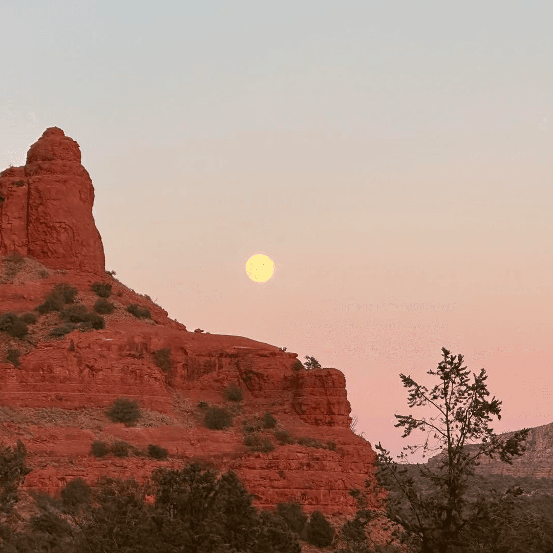 A full moon rises above red rock formations during sunset.