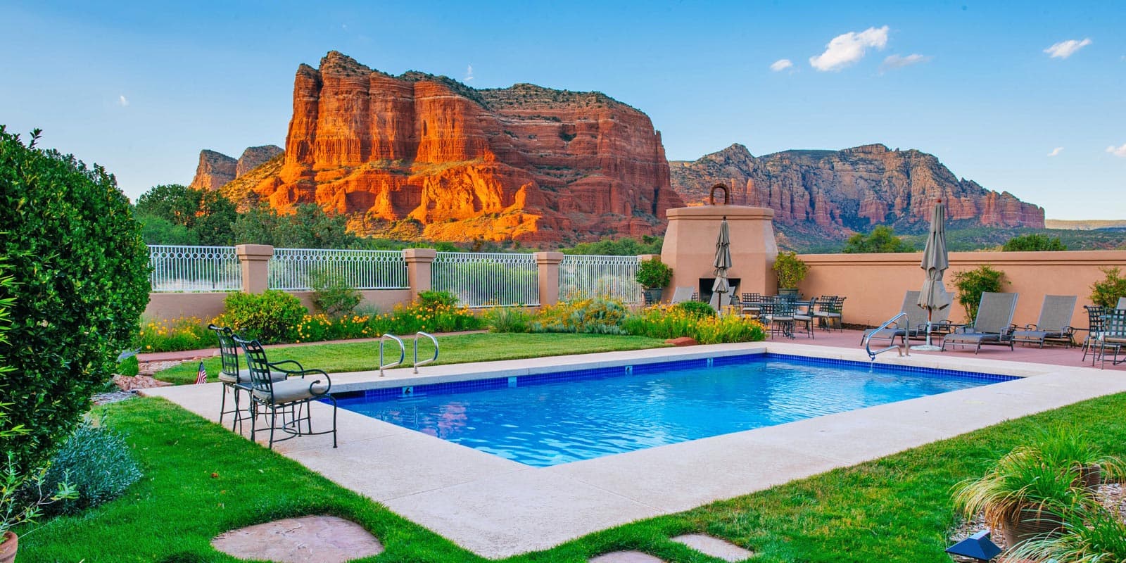 A serene pool area surrounded by lush greenery and striking red rock formations in the background.